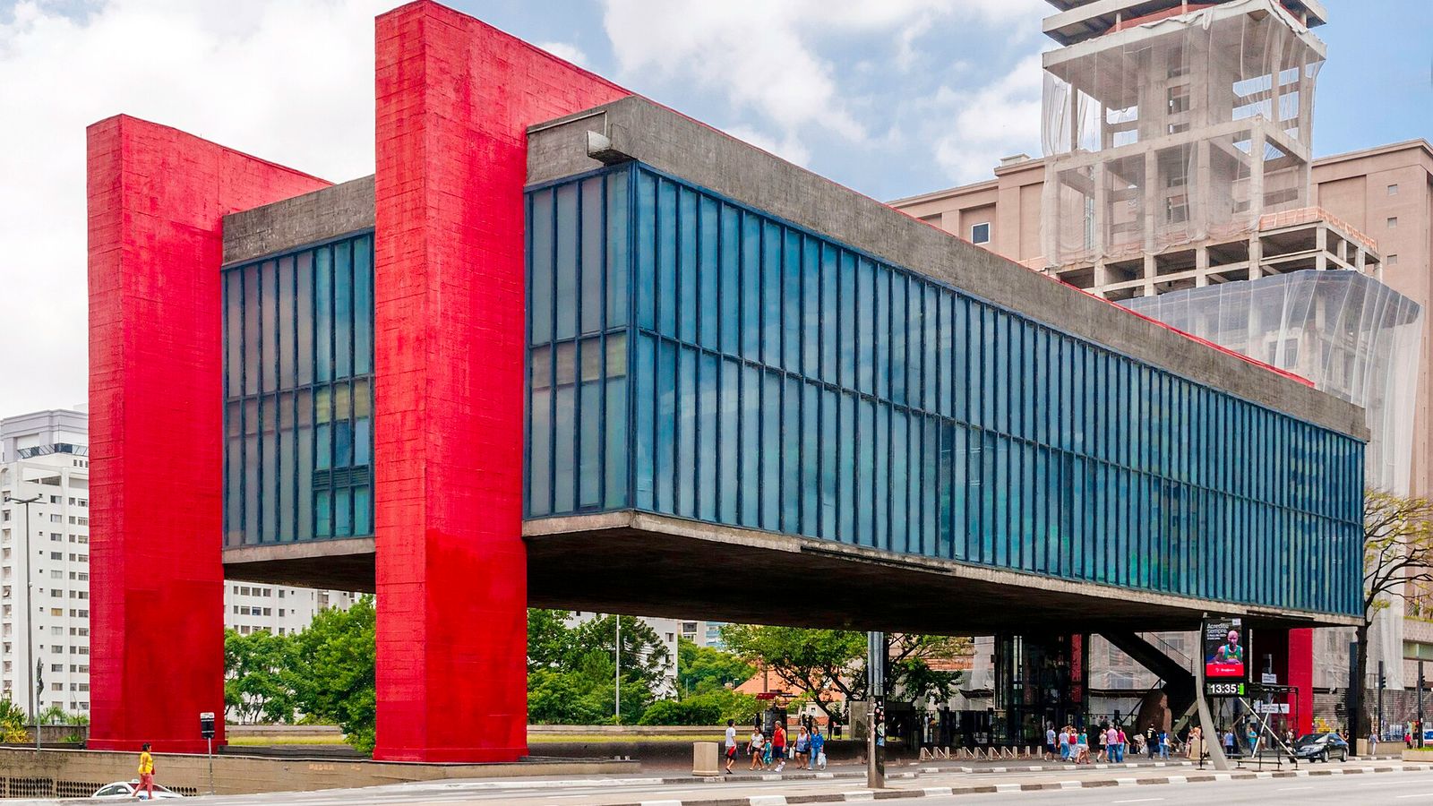 MASP, de Lina Bo Bardi MASP visto da Avenida Paulista: bloco de concreto e vidro suspenso por dois pórticos vermelhos sobre o vão livre