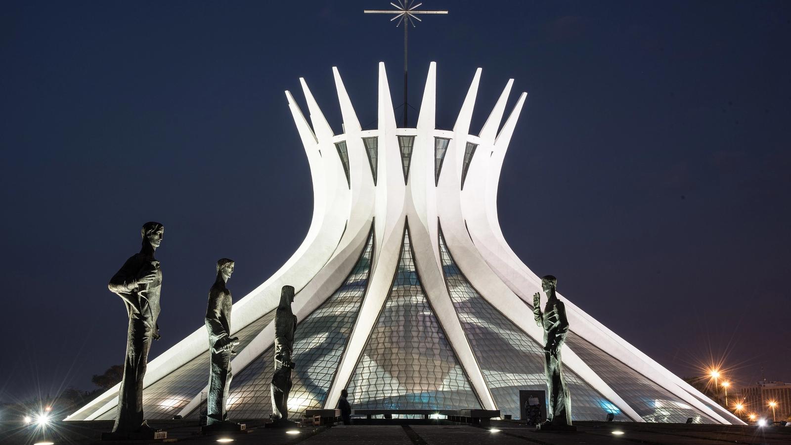 Catedral de Brasília, de Oscar Niemeyer Catedral de Brasília iluminada à noite, com as colunas curvas de concreto e quatro estátuas de bronze dos evangelistas na praça em primeiro plano