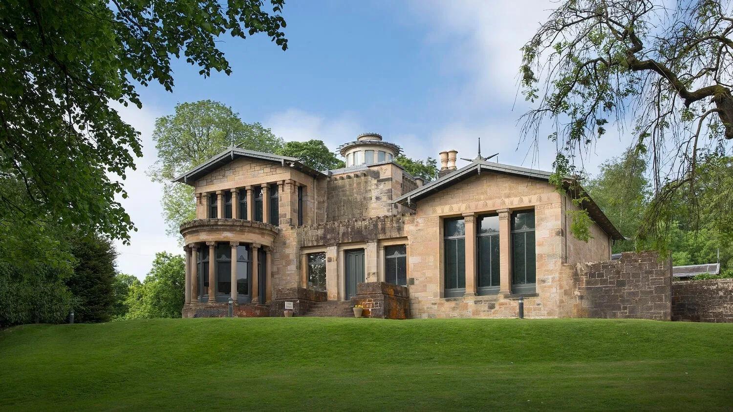 Holmwood House Casa de pedra clara com colunas, janelas altas e torre baixa, cercada de gramado e árvores