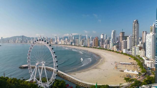 Foto da orla de Balneário Camboriú, aparecendo predios, praia e roda gigante da cidade.