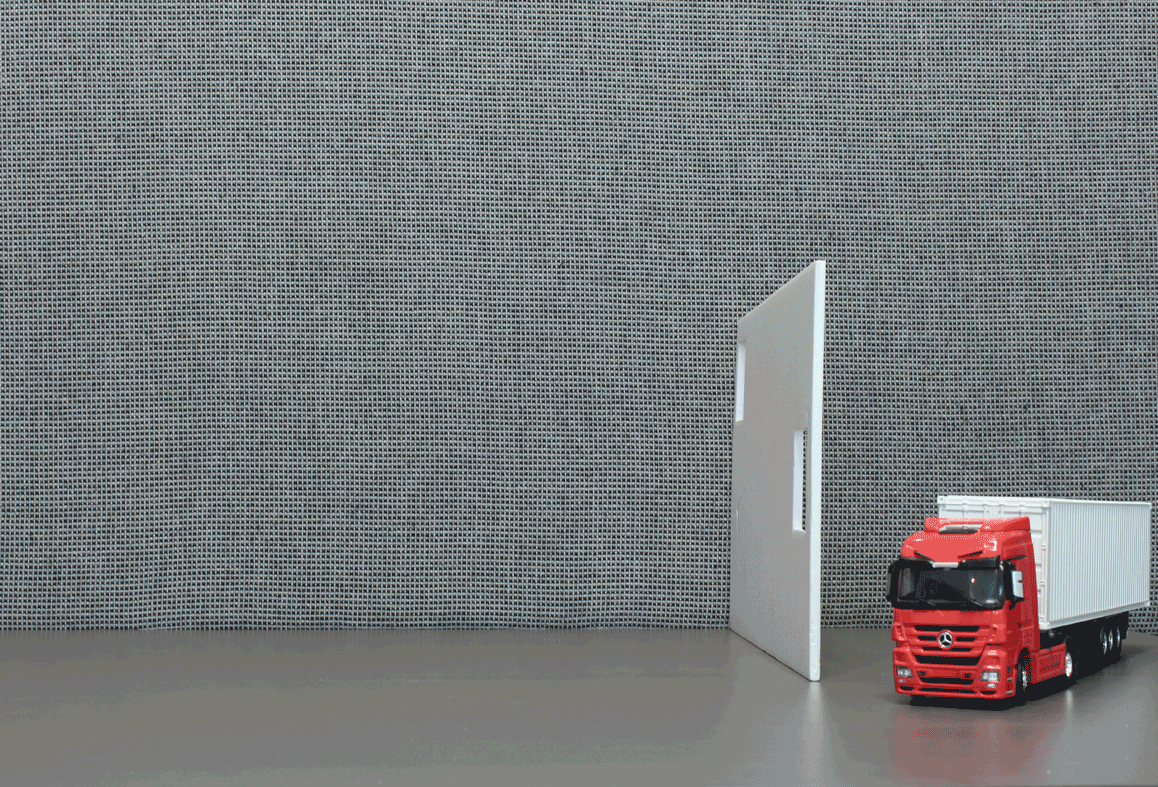 Transporte de módulos pré-fabricados Animação com miniatura de caminhão ao lado de um painel branco sobre fundo cinza, ilustrando o transporte de peças pré-fabricadas