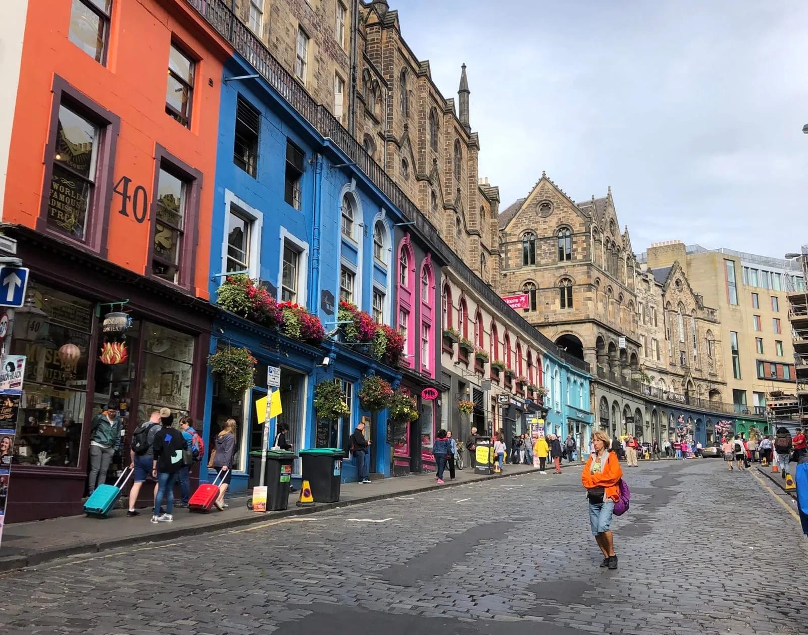 Victoria Street em curva, com lojas de fachadas pintadas em vermelho, azul, rosa e verde e prédios de pedra acima
