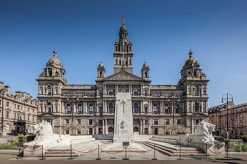Fachada monumental de pedra clara com torre central e esculturas, vista da praça