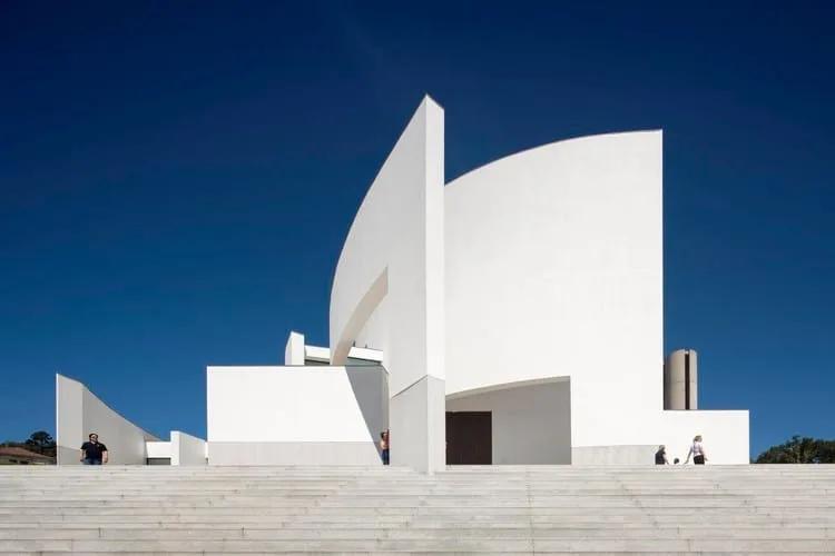 Igreja de paredes curvas brancas no alto de uma escadaria, sob céu azul