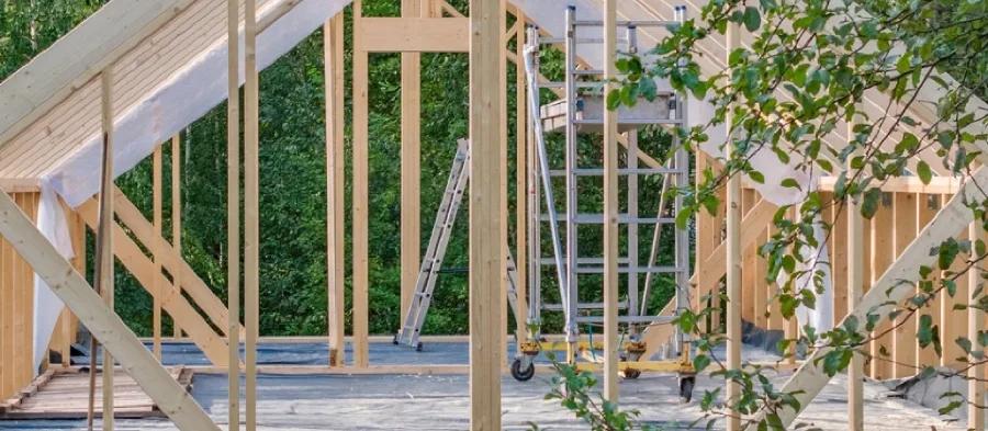 Montagem de estrutura em wood frame no canteiro Obra em wood frame com montantes de madeira em pé, andaime e vegetação ao redor