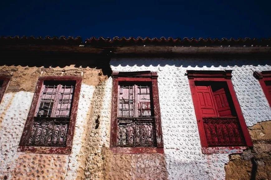 Fachada antiga de parede de terra caiada com janelas de madeira pintadas de vermelho