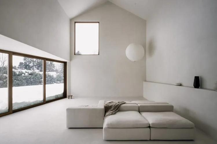 Formas geométricas puras Sala branca com pé-direito alto, teto inclinado, sofá modular baixo e janela de vidro para a neve