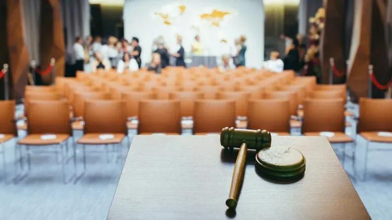 Sala de leilão com cadeiras laranja enfileiradas e martelo de leiloeiro sobre mesa em primeiro plano