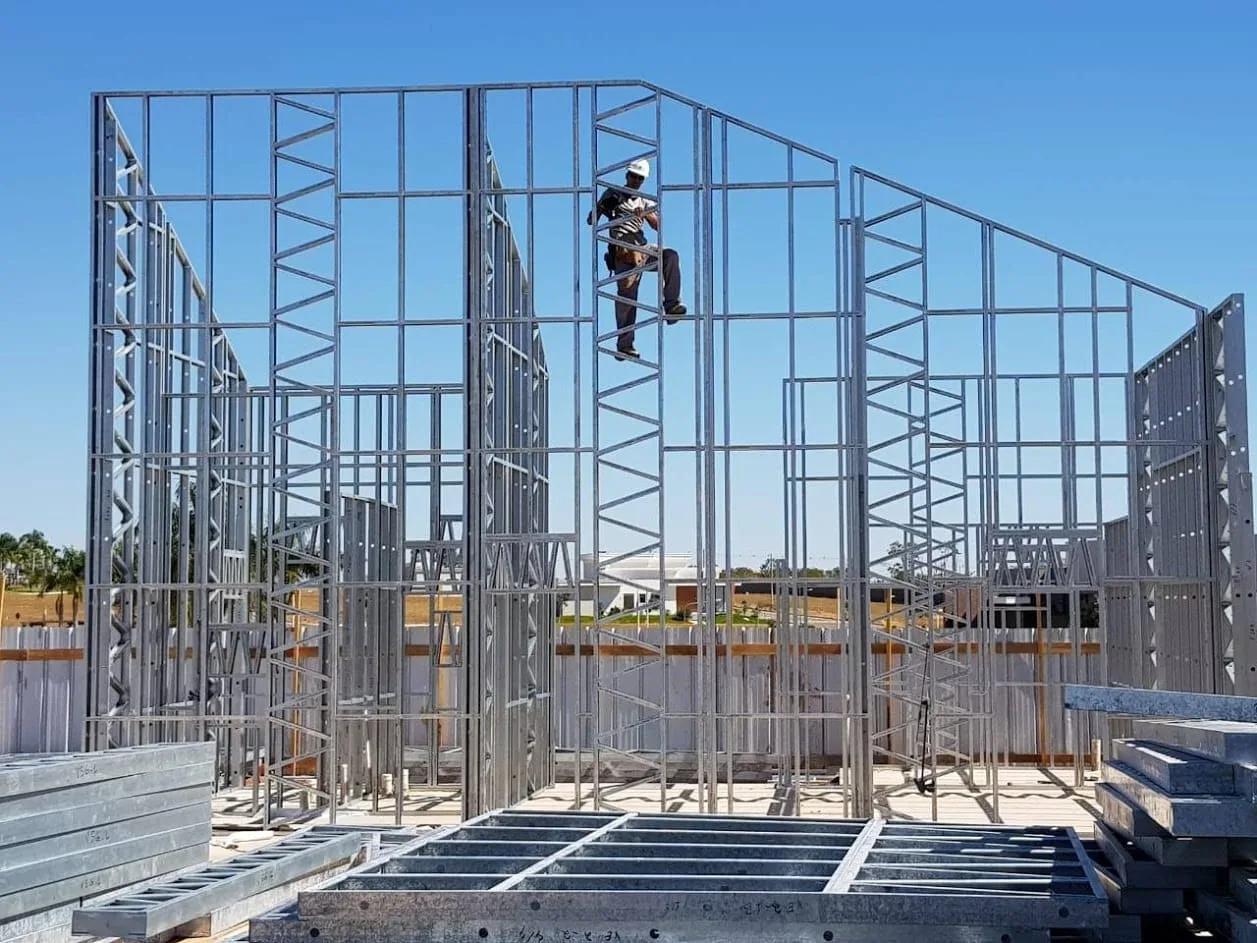 Operário sobre painéis de steel frame em montagem, com perfis empilhados no canteiro