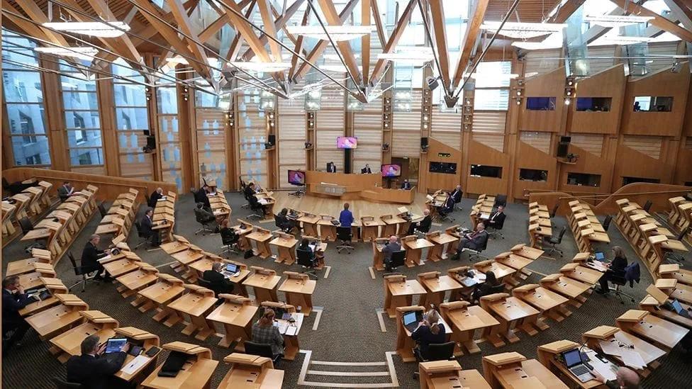 Plenário do Parlamento Escocês com bancadas de madeira em semicírculo e a cobertura de vigas de madeira laminada