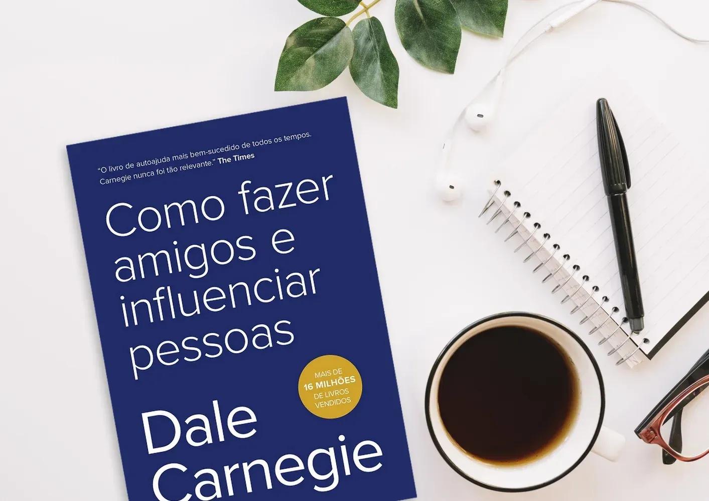 Como fazer amigos e influenciar pessoas, de Dale Carnegie Livro Como fazer amigos e influenciar pessoas, de Dale Carnegie, sobre uma mesa ao lado de xícara de café, caderno e caneta