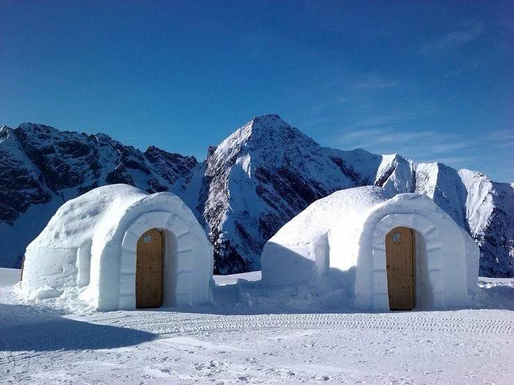 Dois iglus de neve com portas de madeira diante de montanhas nevadas