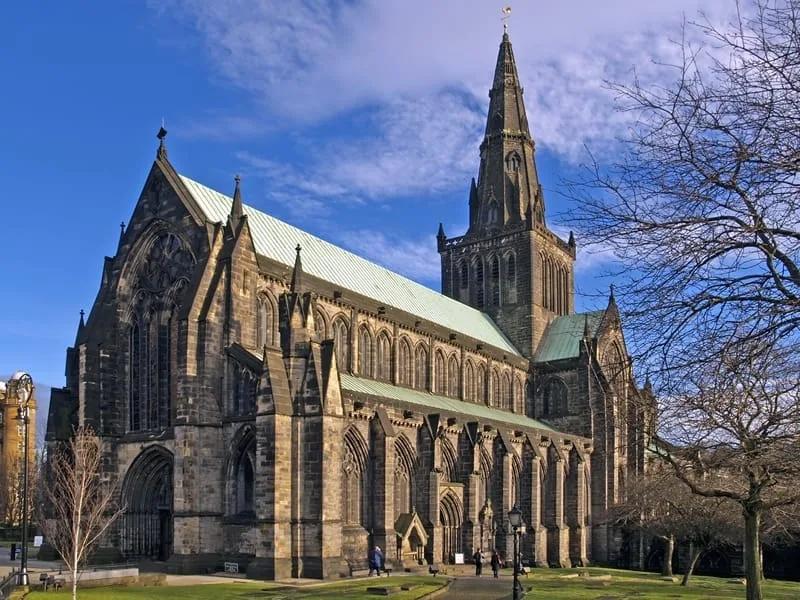Catedral de Glasgow Catedral gótica de pedra escura com torre pontiaguda, cercada por árvores