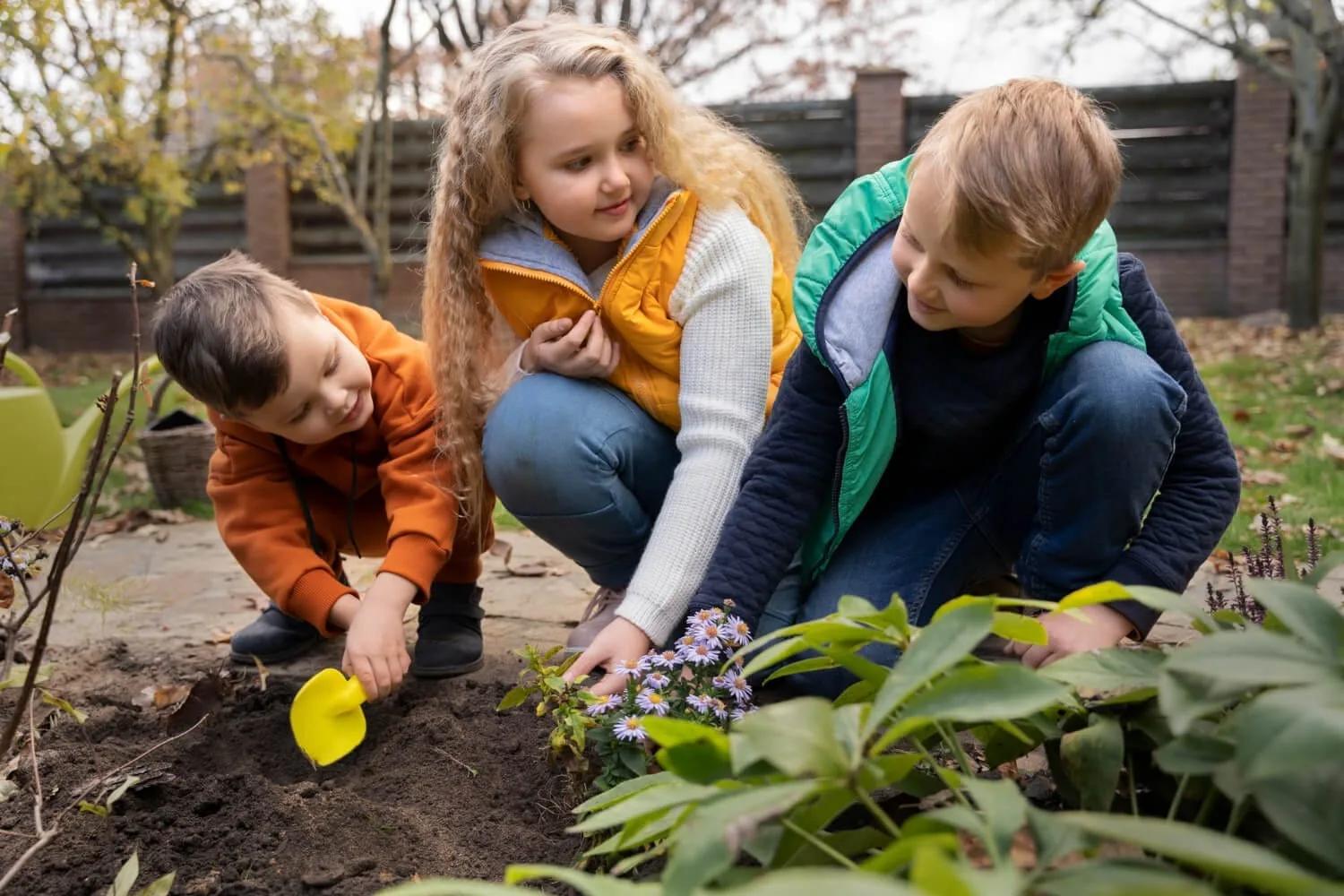Três crianças plantando mudas num canteiro, com terra nas mãos