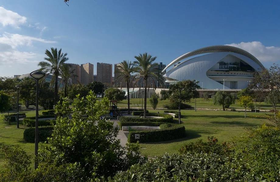 Palmeiras e jardins no antigo leito do Túria com um edifício branco de cobertura curva da Cidade das Artes e das Ciências ao fundo