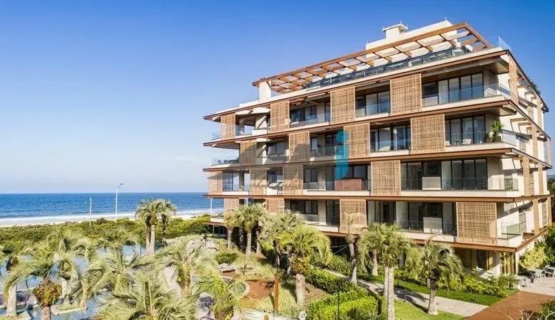 Prédio residencial na Praia Brava Prédio residencial baixo de fachada com painéis de madeira e terraços, entre coqueiros, com o mar ao fundo, na Praia Brava