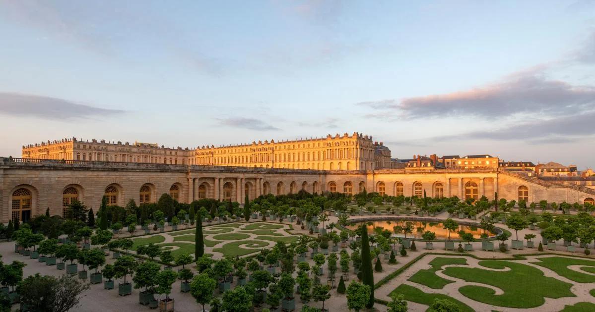 Jardins do Palácio de Versalhes com canteiros geométricos diante de uma longa fachada