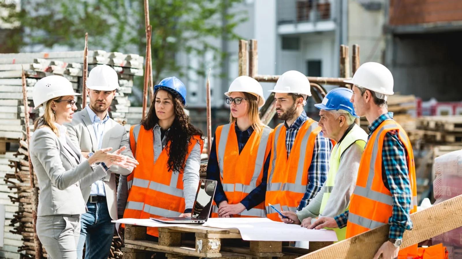 Equipe técnica na obra Equipe de arquitetos e engenheiros com capacetes e coletes em um canteiro de obras, conversando diante de plantas abertas