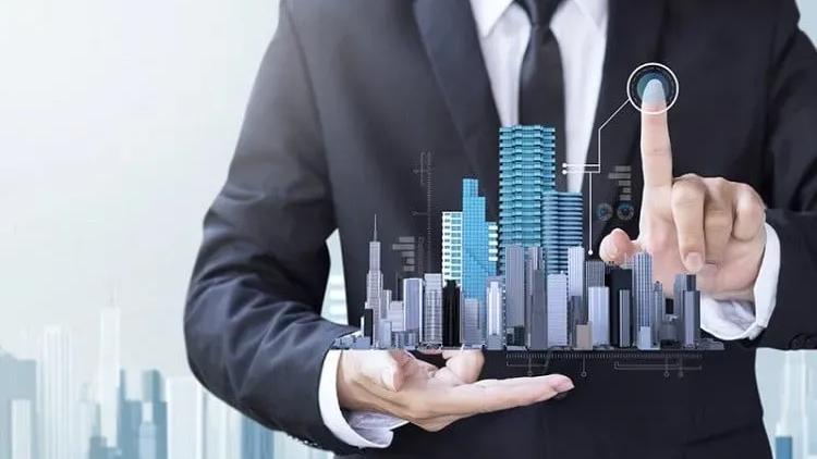 Homem de terno segura na palma da mão uma maquete digital de prédios comerciais e toca um ícone flutuante com a outra mão