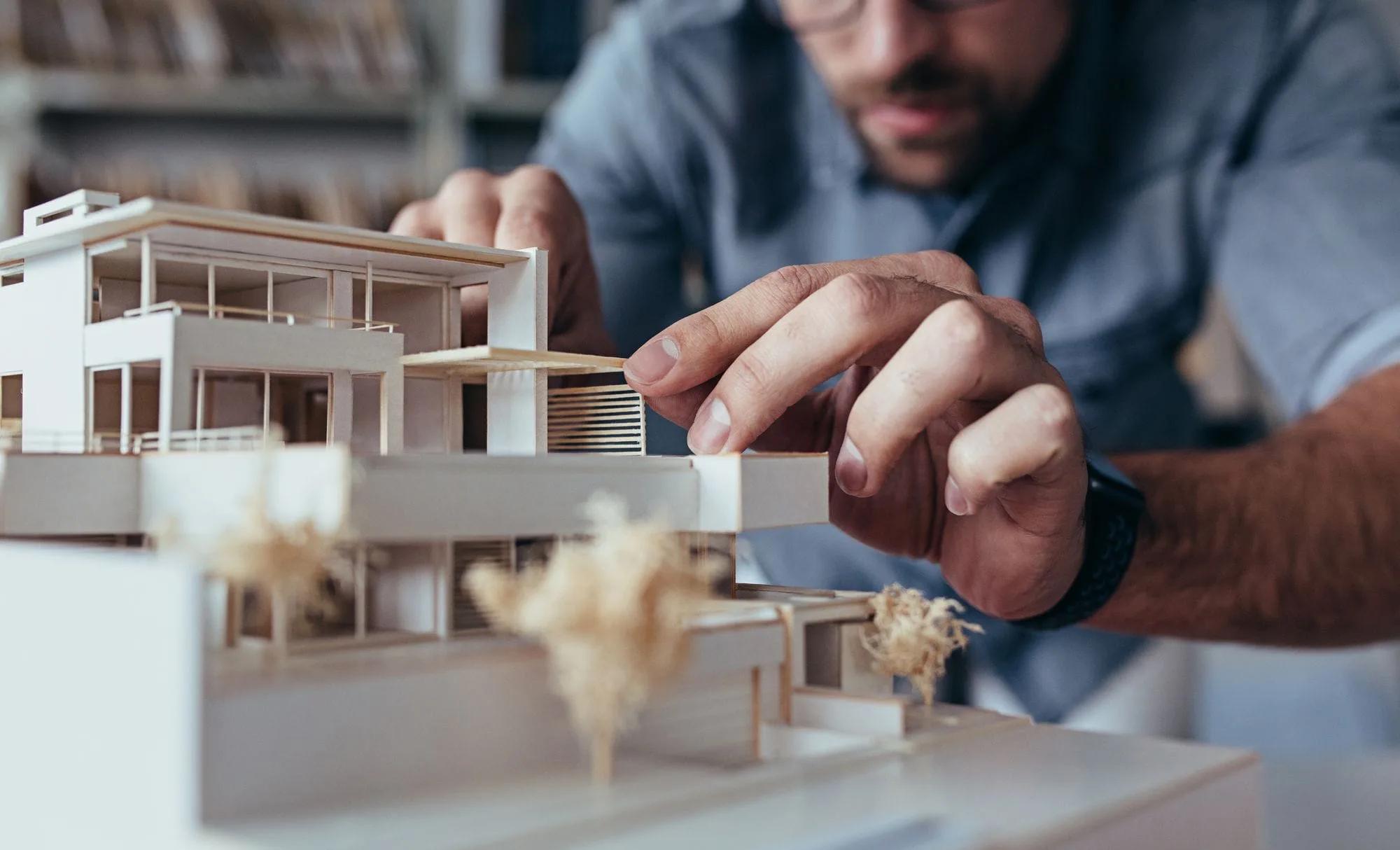 Arquiteto ajustando uma maquete branca de edifício residencial sobre a mesa de trabalho