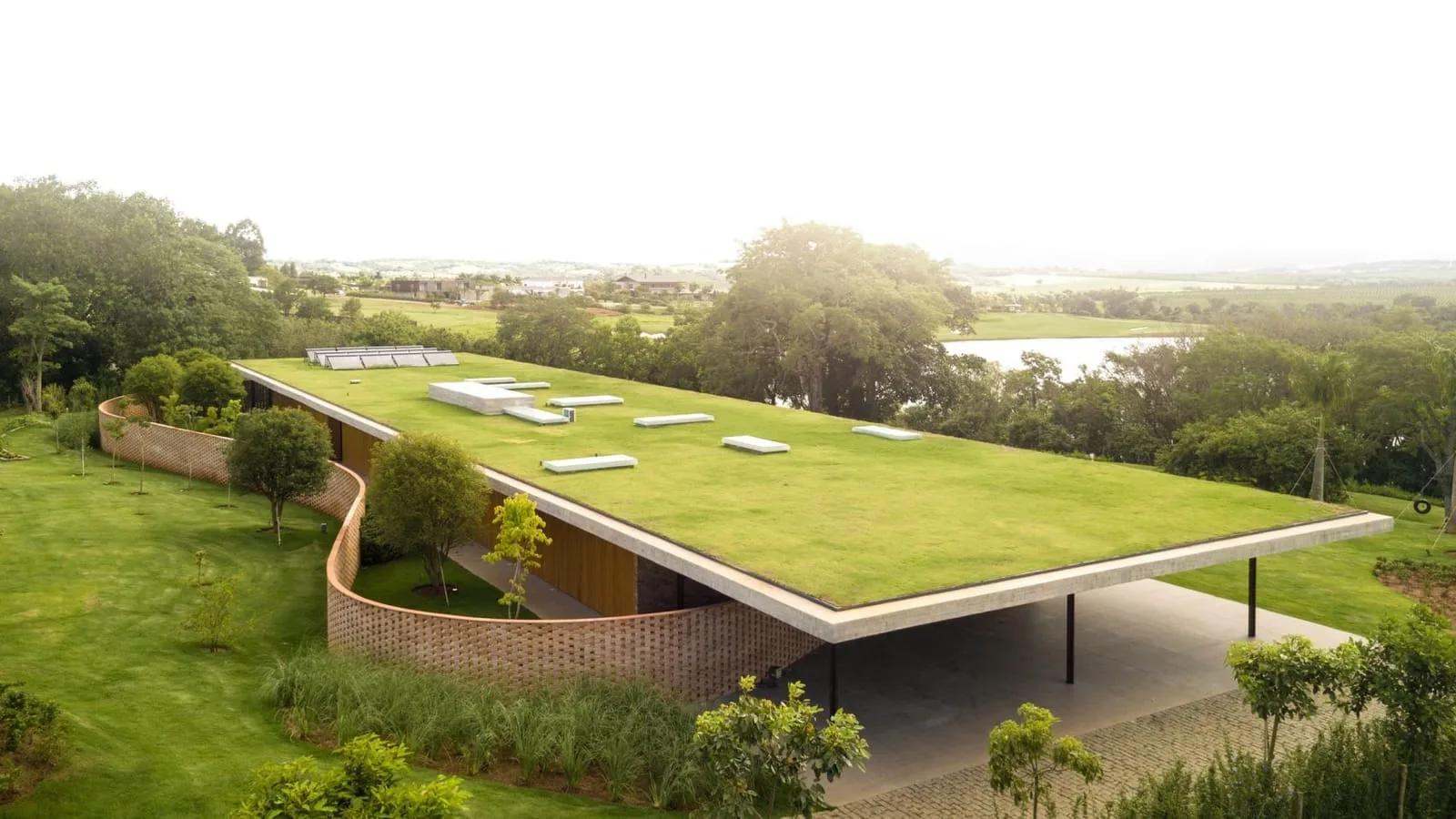 Casa térrea com cobertura verde plana, muros de pedra e grandes aberturas, em meio à vegetação