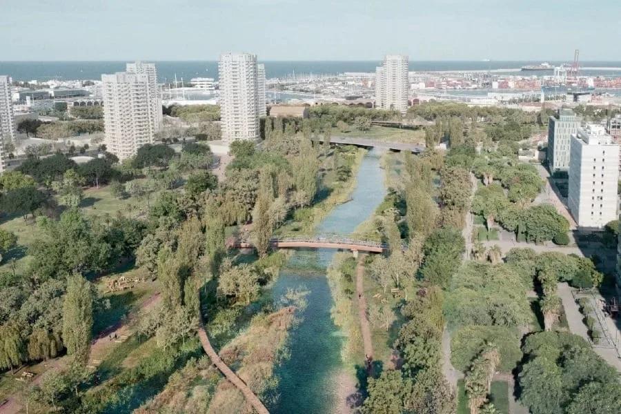 Vista aérea do antigo leito do Túria com canal de água, vegetação, passarelas e prédios altos ao fundo perto do mar