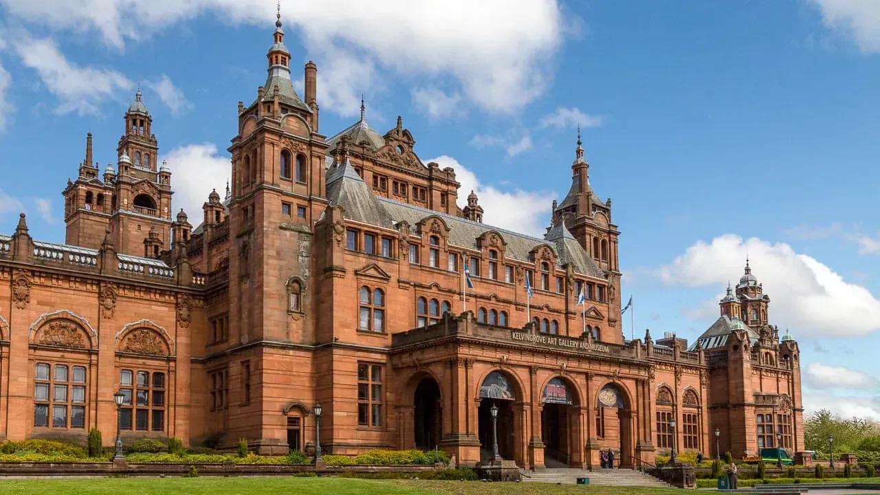 Kelvingrove Museu de arenito vermelho com torres ornamentadas e entrada monumental, entre árvores