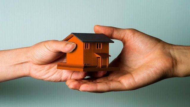 Uma mão passando a maquete de uma casa para outra mão.