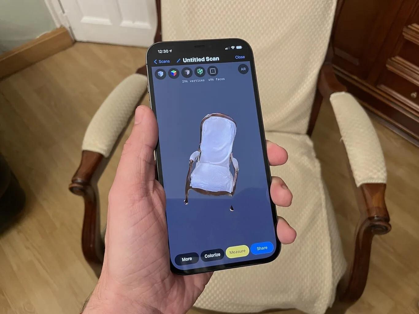 Mão segurando um iPhone que mostra o modelo 3D escaneado de uma poltrona, diante da poltrona real