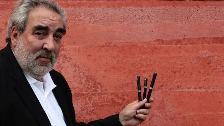 Eduardo Souto de Moura segura canetas diante de uma parede de concreto vermelho
