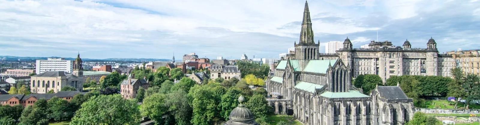 Vista panorâmica de Glasgow com a catedral, a torre gótica e prédios históricos entre árvores