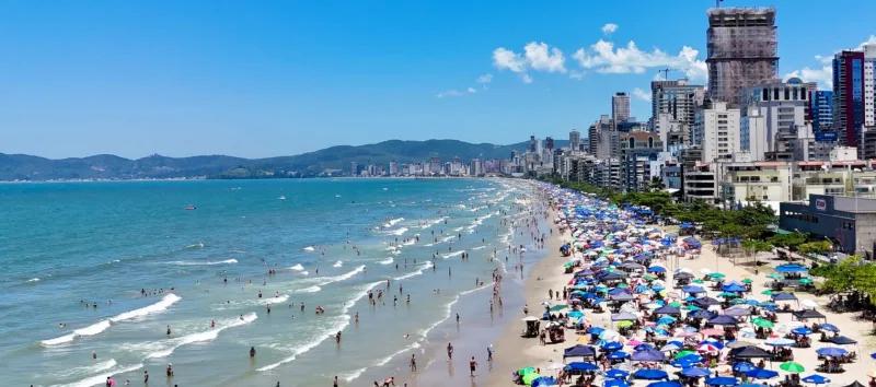 Praia de Itapema lotada de guarda-sóis, com prédios altos na orla e um edifício em construção