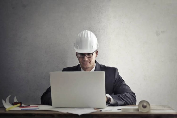 Engenheiro de capacete de obra branco mexendo no computador fazendo curso online.