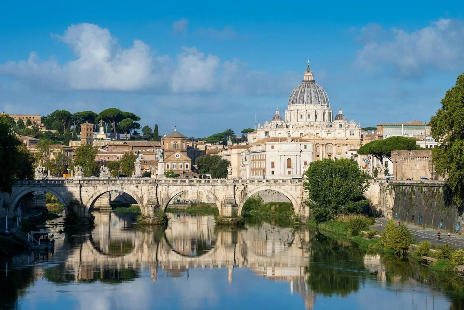 Basílica de São Pedro vista da margem do rio Tibre, em Roma, com ponte de pedra refletida na água