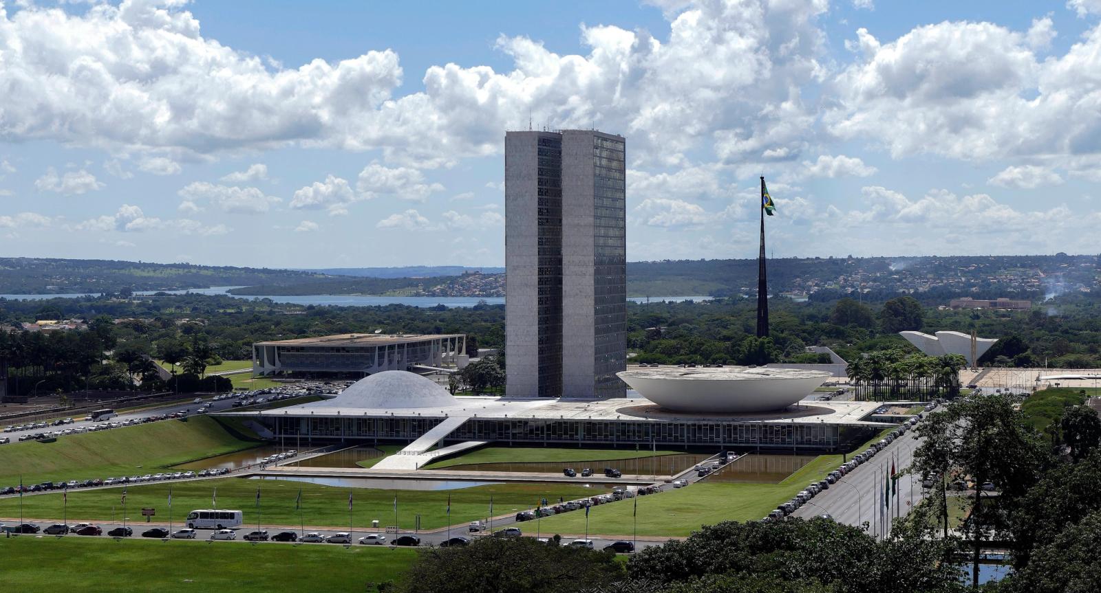 Vista do alto do Congresso Nacional: duas torres no centro, a cúpula menor à esquerda e a cúpula invertida, maior, à direita, com o lago Paranoá ao fundo