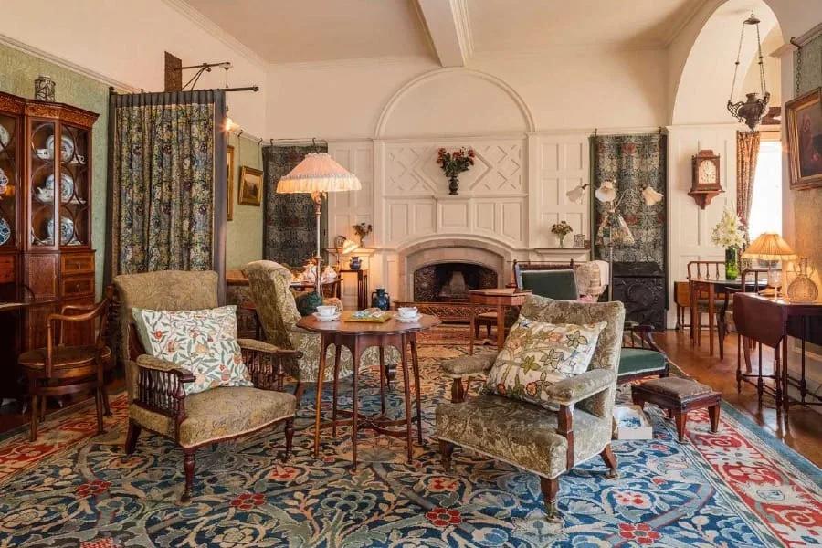 Standen House Sala de estar com lareira, poltronas estampadas, tapete, lustres e armários de madeira