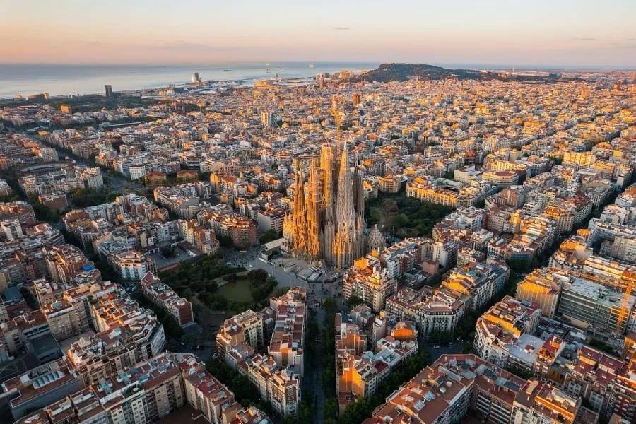 Barcelona: a Sagrada Família e a malha do Eixample Vista aérea de Barcelona com a Sagrada Família no centro, cercada pelas quadras regulares do Eixample, e o mar ao fundo