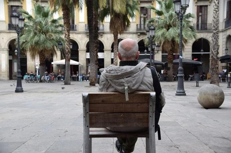 Banco individual isolado em uma praça, com mesas de bares e restaurantes ocupando o fundo da imagem