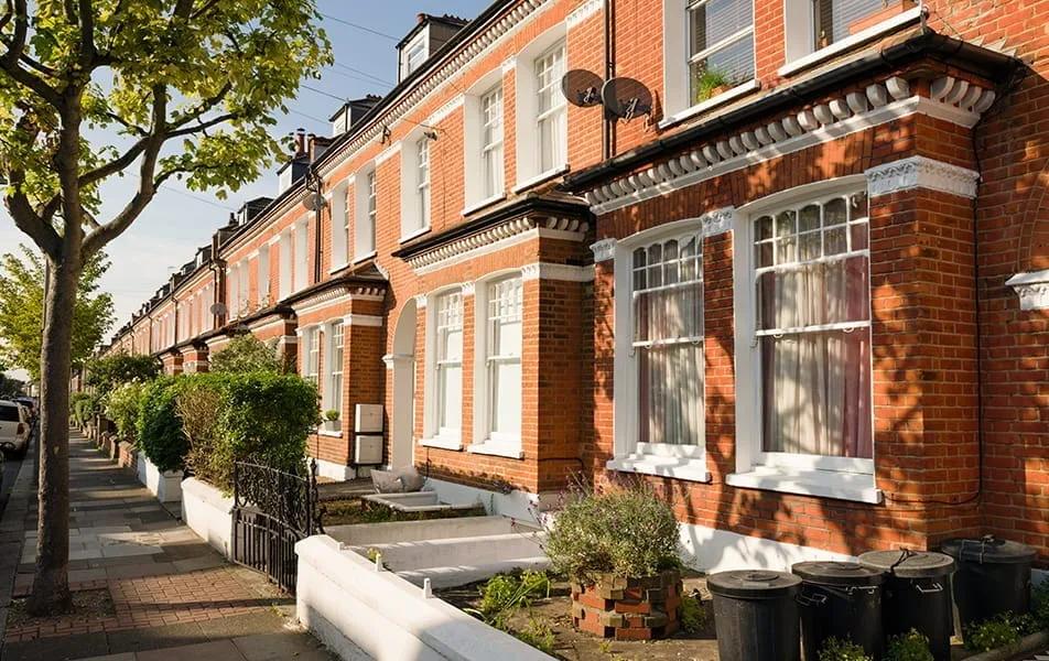 Rua residencial britânica com casas geminadas de tijolo vermelho, janelas salientes brancas e jardins na frente