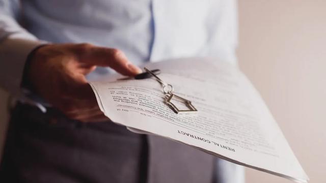 Mão segurando contrato de aluguel e chaveiro do imóvel a ser alugado.