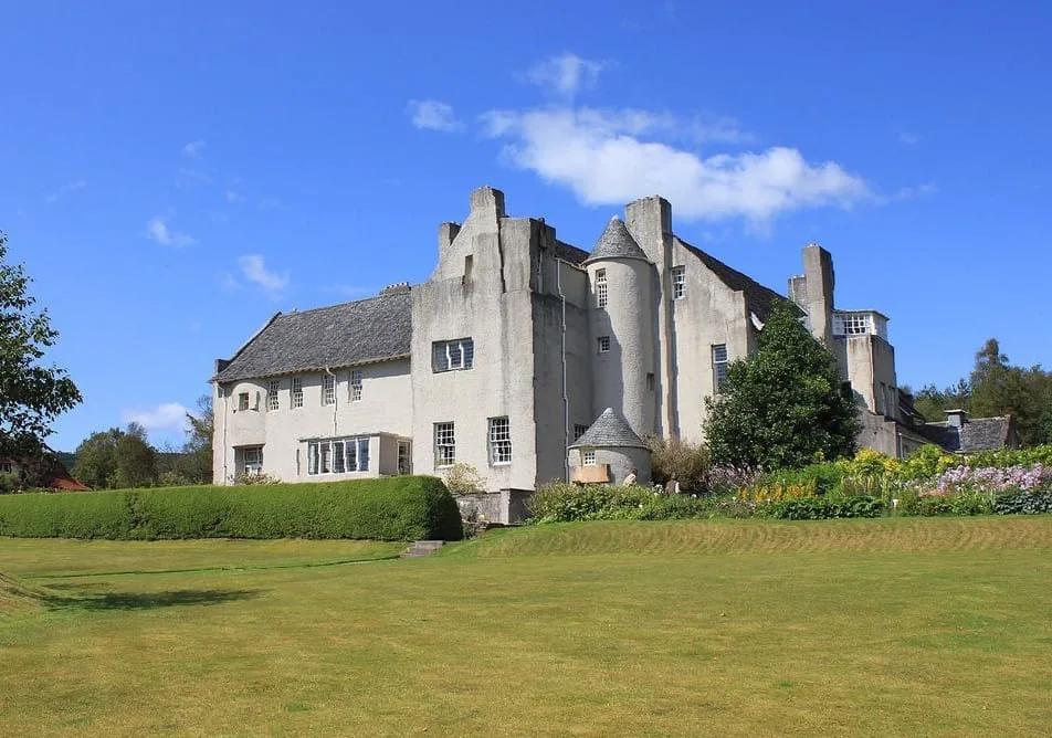 The Hill House, Helensburgh Fachada branca da Hill House, em Helensburgh, com volumes simples, telhados inclinados e uma torre cilíndrica, vista de um gramado