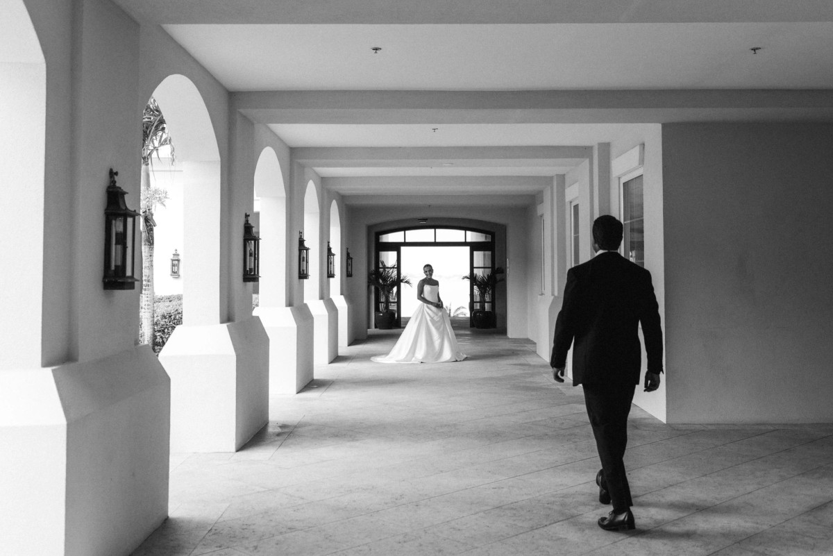 Groom walking toward the bride down a long arched colonnade at Rosewood Bermuda, black and white