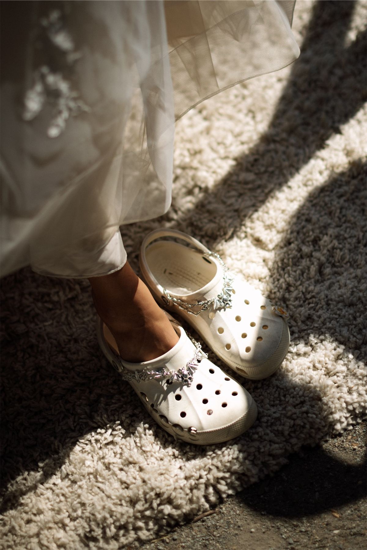 Detail of a lace gown hem falling over white Crocs on gravel