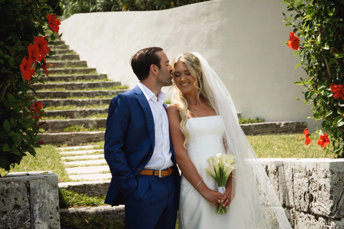 Cam kisses Paige's cheek in front of the stone garden steps and hibiscus on Hawkins Island, Bermuda