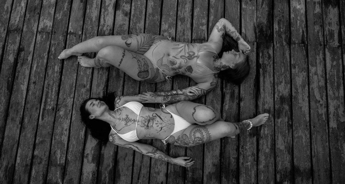 Black and white overhead frame of two models lying side by side on a wooden dock