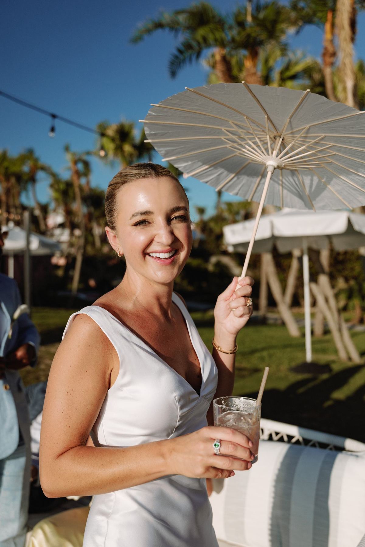 Bride laughing under a paper parasol with a drink in hand at her Bermuda wedding