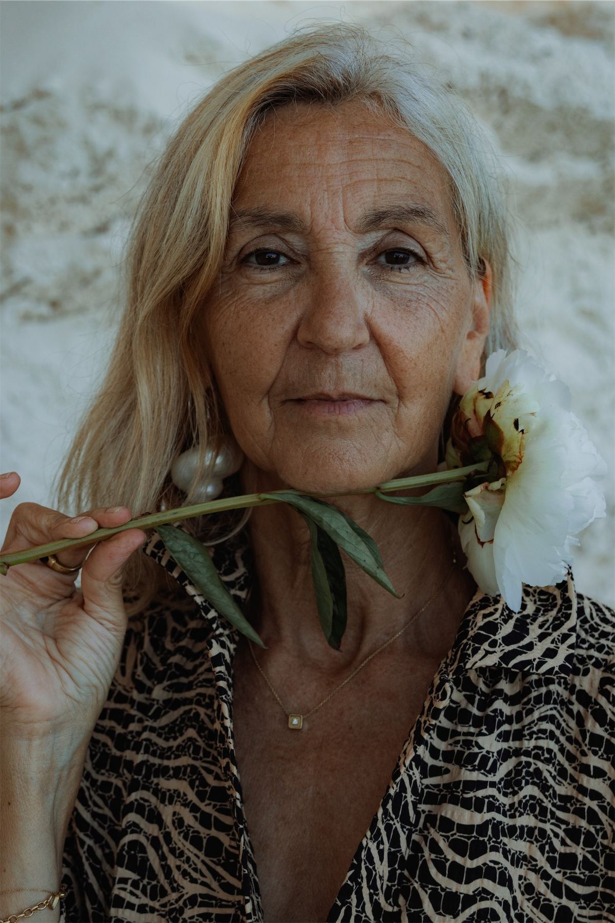 Portrait of a silver haired model in an animal print shirt holding a flower stem