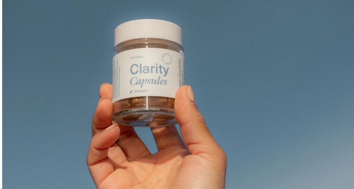Hand holding a jar of Clarity Capsules against a flat blue background
