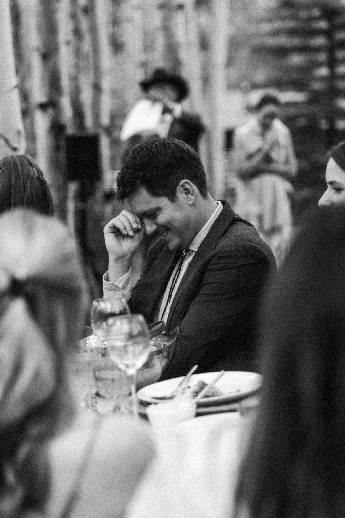 A guest laughs into his hand during a speech at a mountain ranch among the aspens, black and white