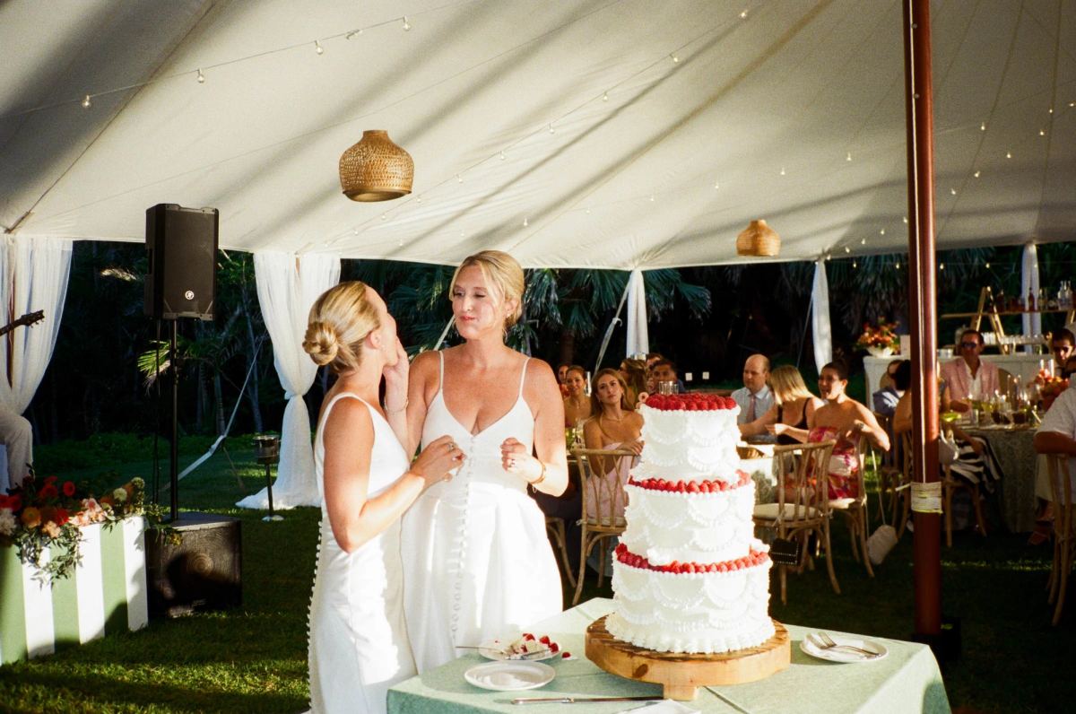 Two brides cutting the wedding cake inside the tent at their Bermuda reception